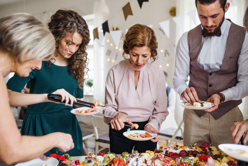 Adultos se servindo no open house junto à mesa de comidas e bebidas.